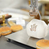 Electric heat stamping machine branding a fresh coconut with a custom logo, with stamped burger buns displayed nearby.